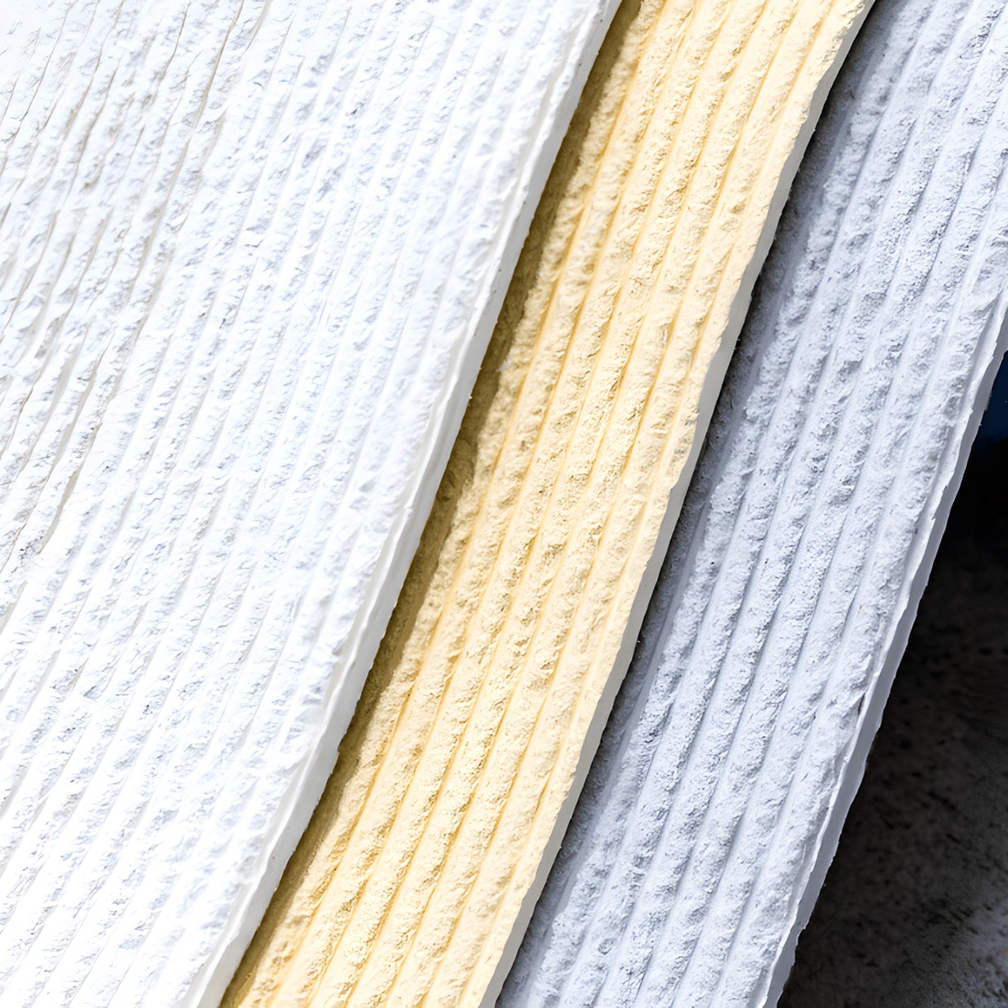 Close-up of three Landmark Decor Cut Stone Sheet - Beige panels in white, pale yellow, and light gray—showcasing the subtle beauty of flexible stone veneers arranged side by side.