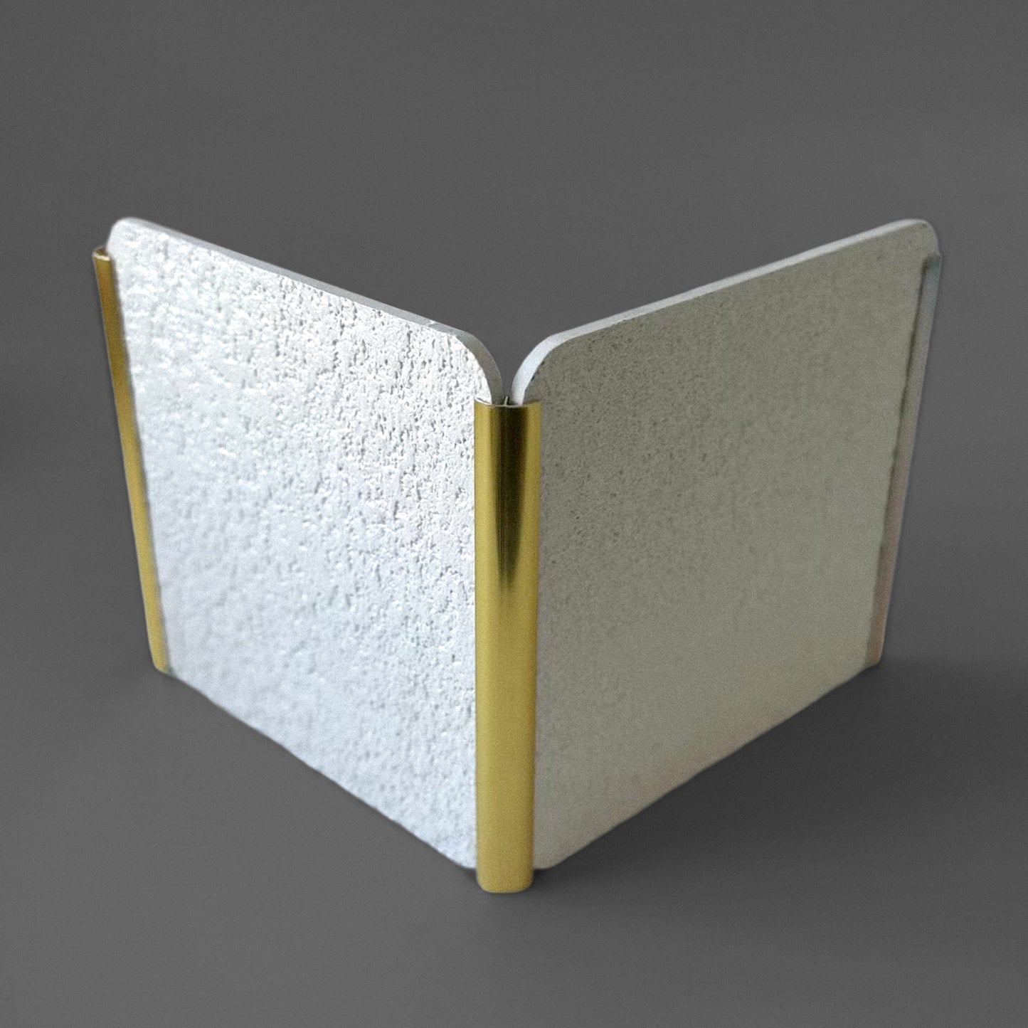 The Landmark Decor PVC Wall Inner Corner Strip features two textured silver panels joined at a right angle by gold-colored cylindrical hinges with precise edges, displayed on a gray surface.