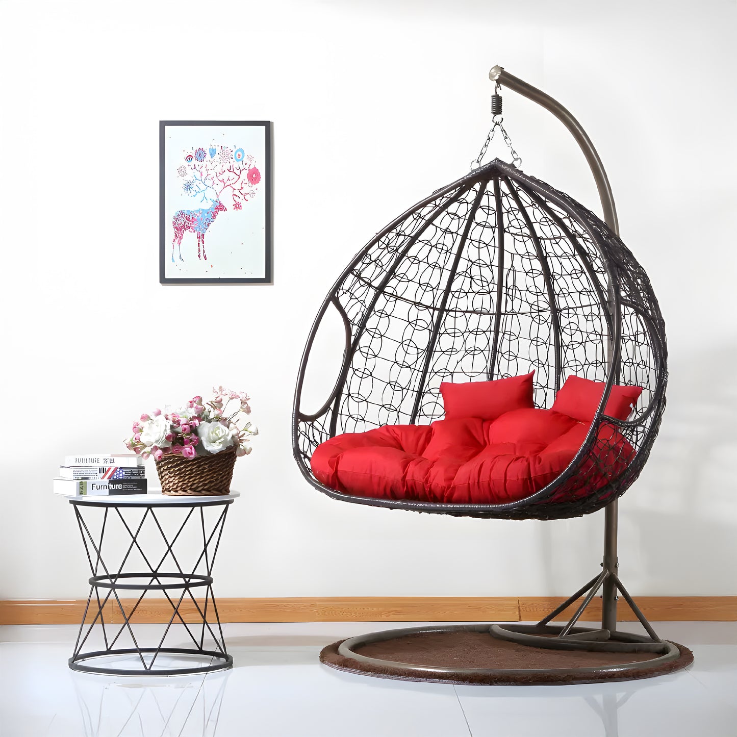 The Soho Outdoor Swing Chair - Black by Landmark Decor, with its luxurious design and red cushions, is elegantly suspended on a metal stand. Nearby, a small round table holds vibrant flowers. A colorful deer and butterfly artwork graces the wall, enhancing the charm of this serene indoor-outdoor retreat.