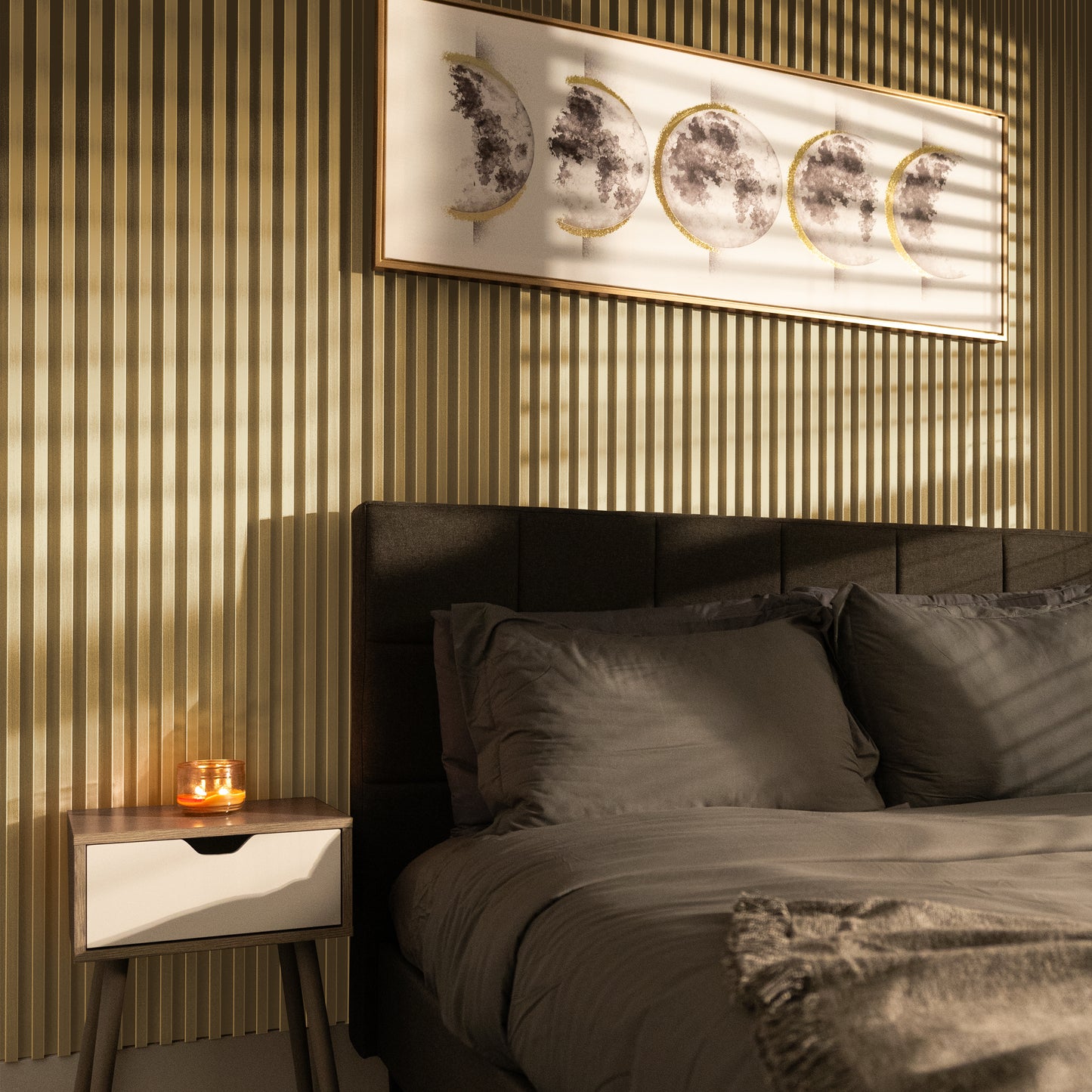 A modern bedroom with a gray bed, a side table with a lit candle, and lunar phase art on Landmark Decor Matte Champaign Gold WPC Fluted Slat Wall Panels, sunlight casting dramatic shadows.