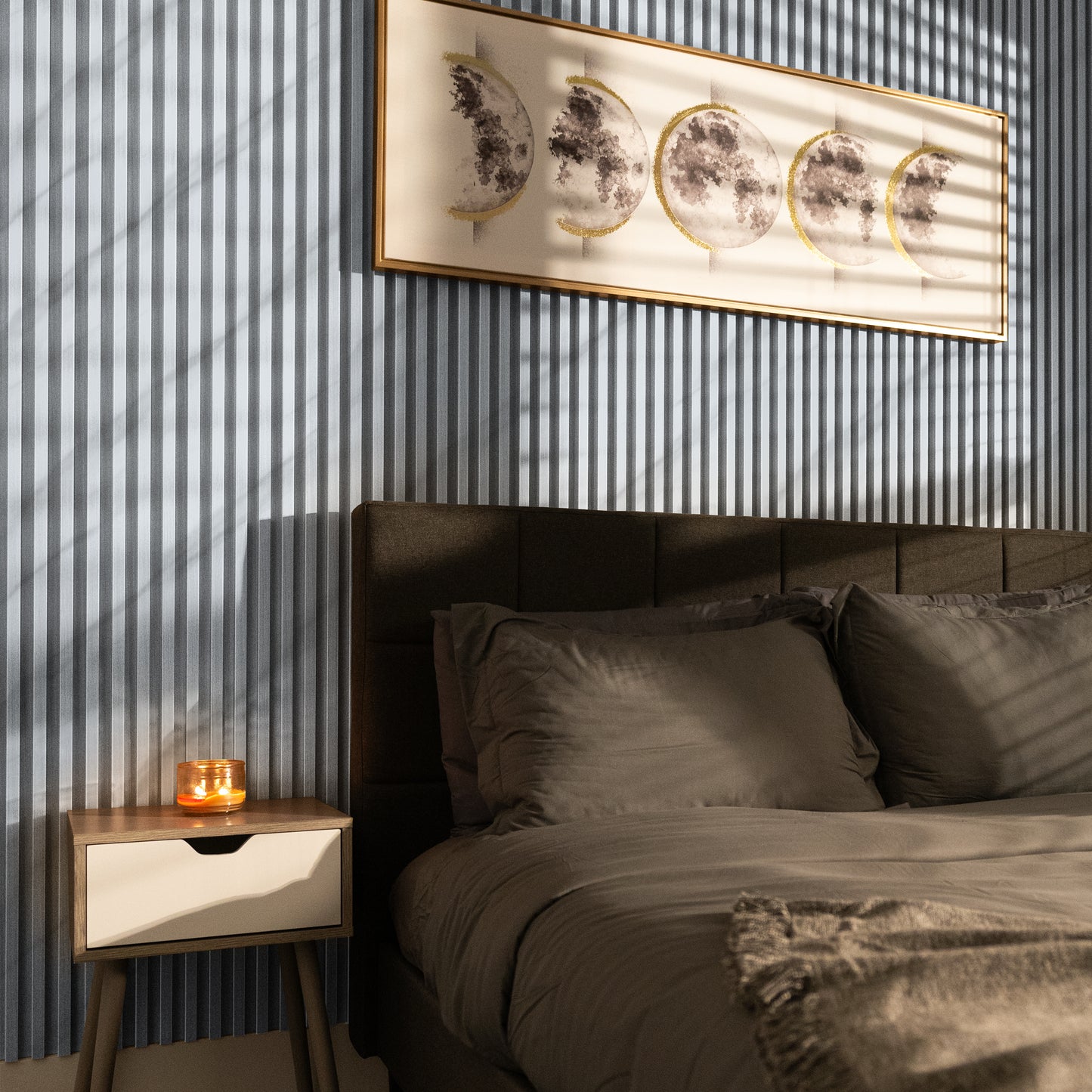 Sunlight casts shadows in a modern bedroom featuring a gray upholstered bed, cozy bedding, and moon phase artwork above, all enhanced by Landmark Decor's Light Smoke WPC Fluted Slat Wall Panels for a serene atmosphere.