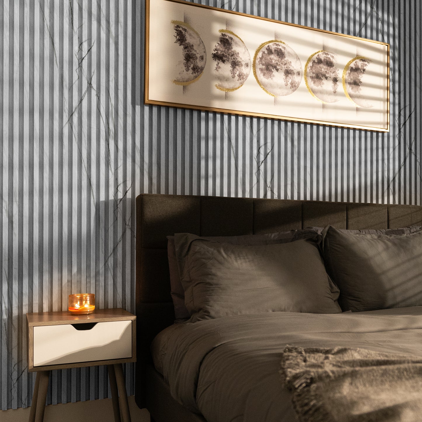 A modern bedroom featuring Landmark Decor’s Silver Crest Marble WPC Fluted Slat Wall Panel as a gray-striped accent, with gray bedding, a nightstand with a lit candle, and moon phase artwork above the bed.