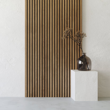 A glass vase with dried branches sits on a white pedestal in front of Landmark Decor's Exterior Wall Panel Keel, set against a white textured background.