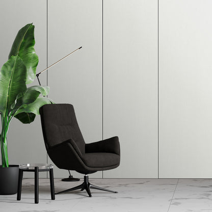 A modern black armchair sits by a leafy potted plant and a small round glass table on a marble floor, set against an Alabaster White Carbon Sheet wall by Landmark Decor with sleek, modern panels.