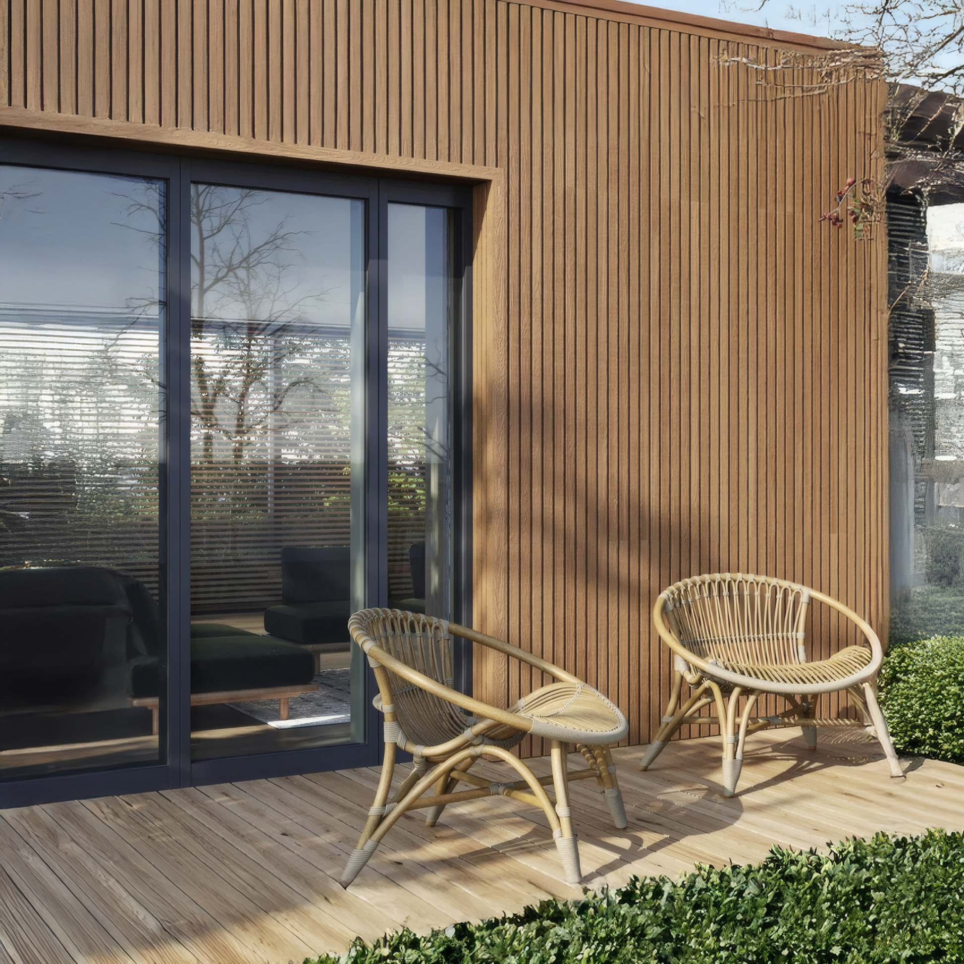 Two wicker chairs sit on a wooden deck outside a modern building with Landmark Decor's Honey Chestnut Exterior Panel Corner, ideal for stylish outdoor use and exterior wall installations beside large glass sliding doors.