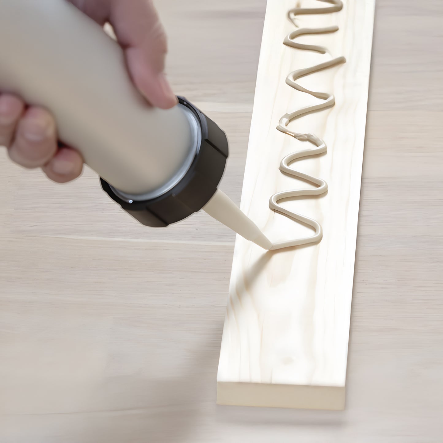 A person uses a caulking gun to apply Landmark Decor Wall Panel Installation Adhesive in a zigzag pattern on a wooden board, prepping it for decorative wall panels or installation.