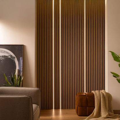 A modern living room featuring Landmark Decor LED Lights, vertical wooden slats, a gray sofa, a brown leather ottoman with a beige blanket, plants, and a framed abstract painting on the floor.