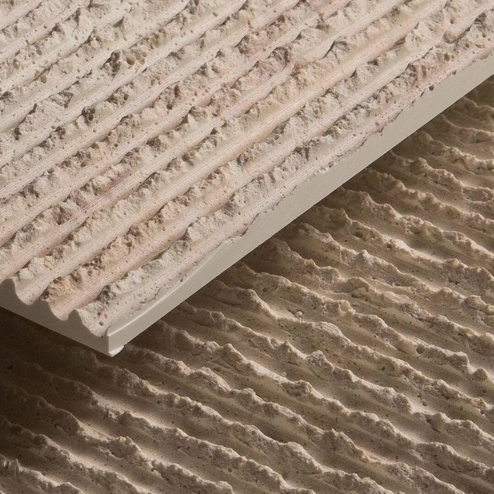 A close-up of two grey, textured Oman Linear Stone Sheets by Landmark Decor, featuring parallel ridges and a natural stone finish, with one sheet stacked slightly above the other.