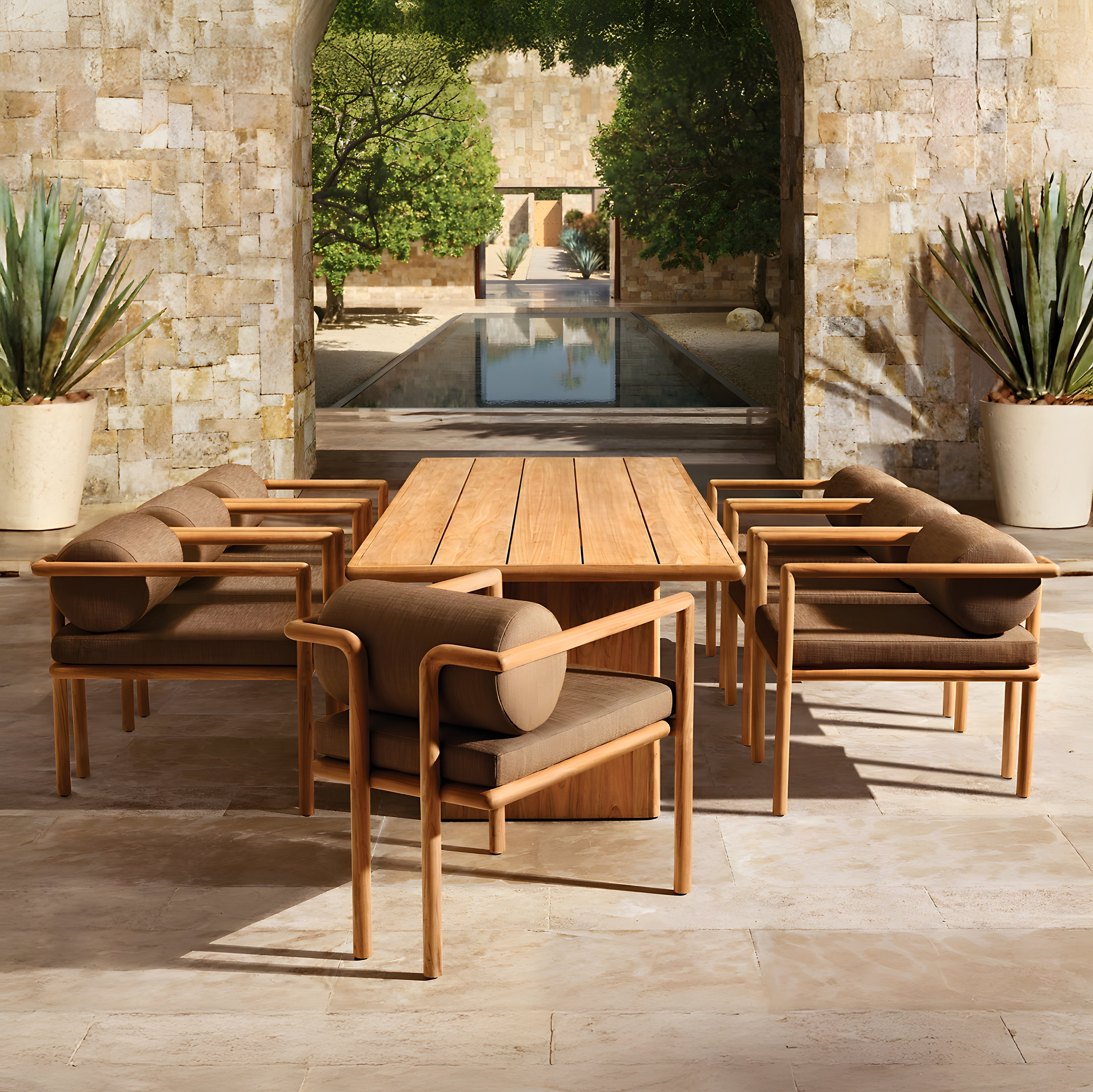 In a stone courtyard, The Hidden Canyon Collection by Landmark Decor features a wooden outdoor dining table made from weather-resistant materials and cushioned chairs. An archway opens to a tree-lined pool view with a stone pathway, creating an ideal setting for serene alfresco dining.