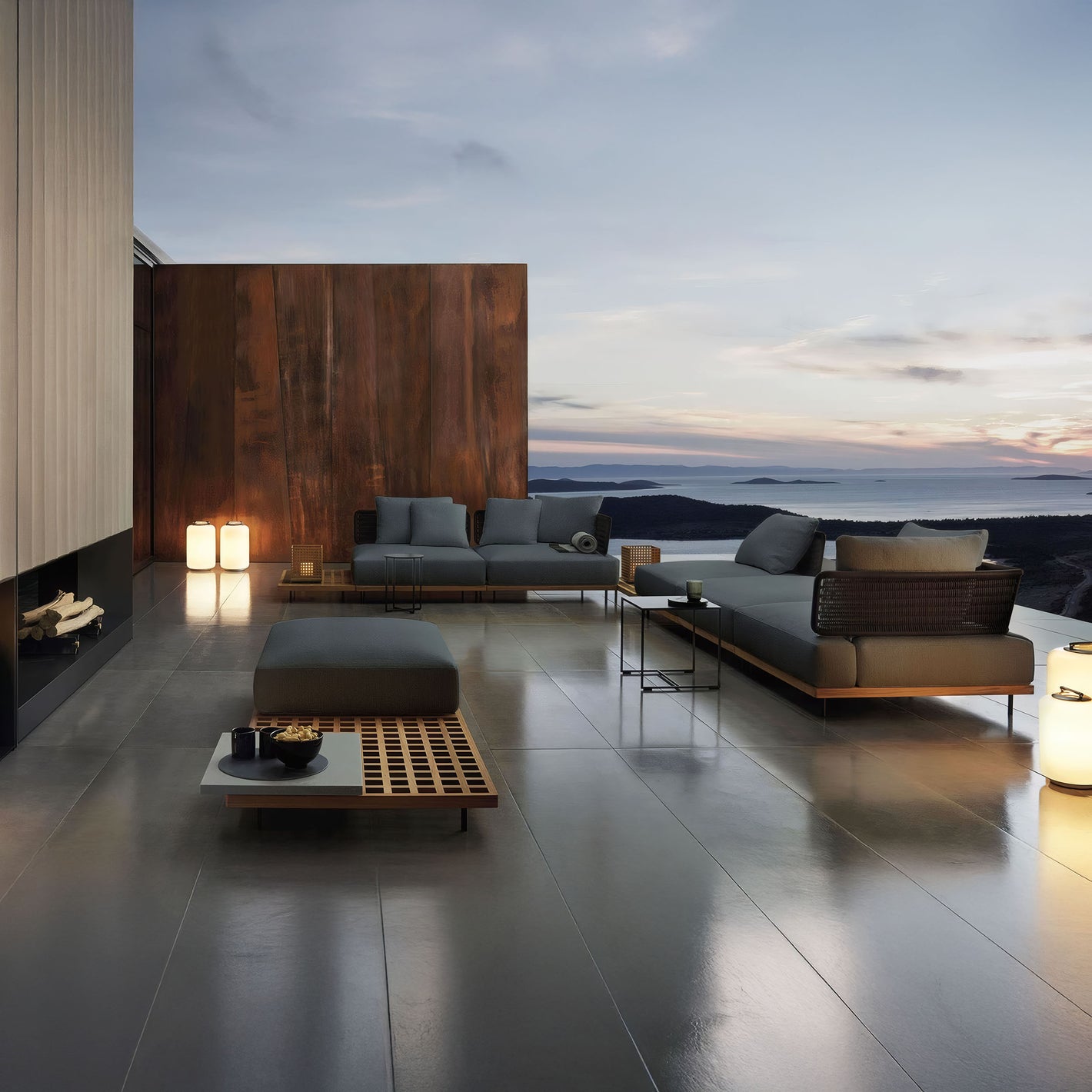 The Oceanview Oasis Collection by Landmark Decor offers sleek gray seating with wooden tables against a wooden accent wall. Weather-resistant cushions and lanterns complete the contemporary look, creating a serene setting with scenic sunset views over hills and water.