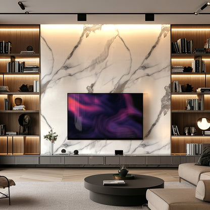 A modern living room with a Calacatta Mist Marble Durable PVC Wall by Landmark Decor, built-in shelves with books and decor, a large flat-screen TV, and a round coffee table.