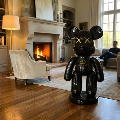 A Landmark Decor Black Bear - Medium sculpture stands as striking interior decor in a living room with a lit fireplace, while a man sits reading on the couch in the background.