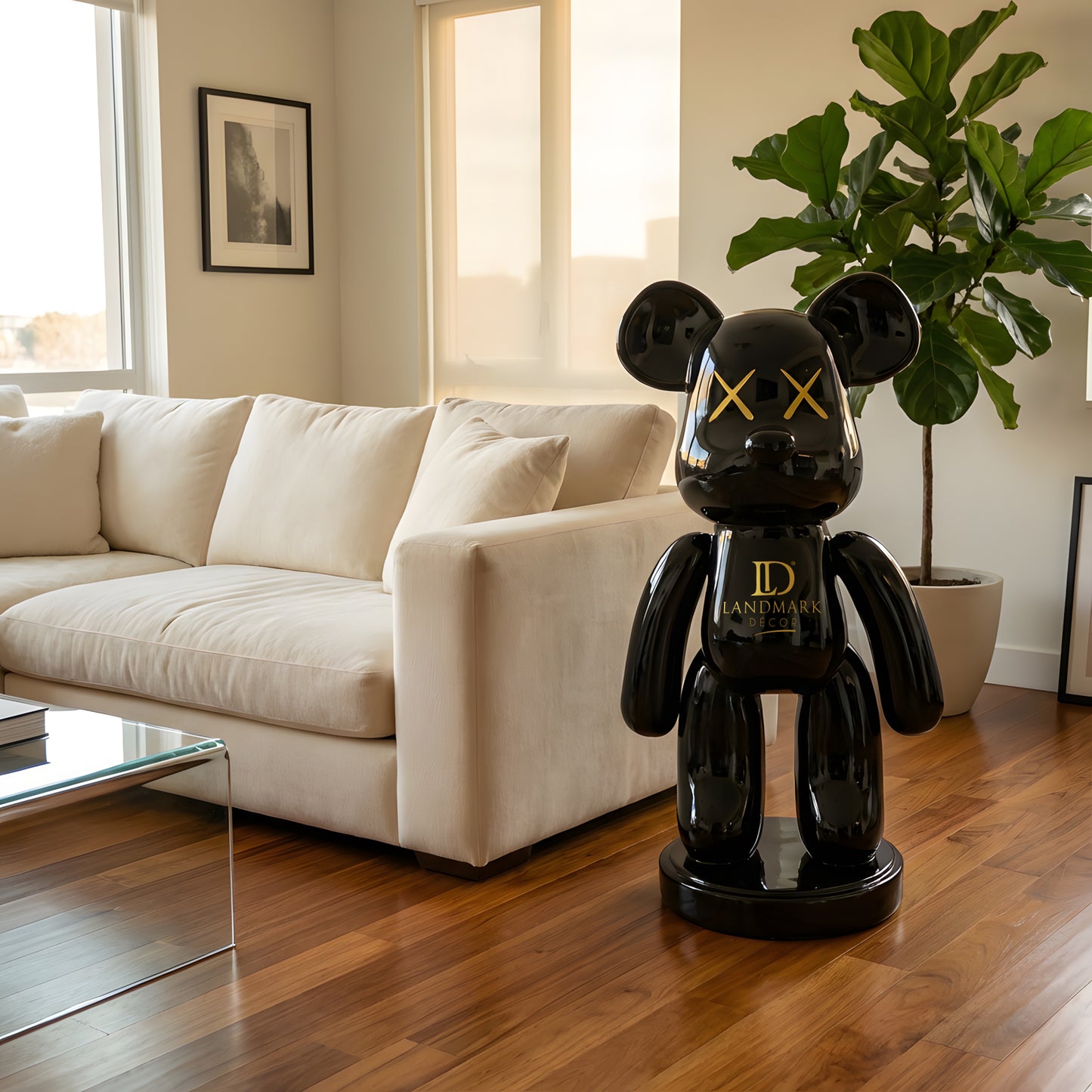 A modern living room featuring a white sofa, leafy plant, and the Landmark Decor Black Bear - Medium sculpture—glossy black with yellow X eyes—adds a bold statement to the decor.