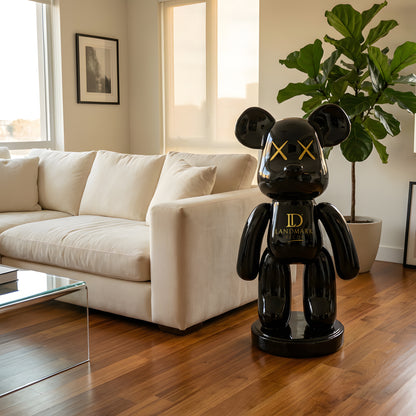 A modern living room featuring a white sofa, leafy plant, and the Landmark Decor Black Bear - Medium sculpture—glossy black with yellow X eyes—adds a bold statement to the decor.