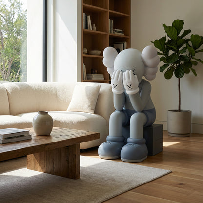 Veiled Thoughts by Landmark Decor, a large cartoon-like sculpture with its face in its hands, serves as striking art and decor on a bench in a modern living room with a sofa, wooden table, bookshelf, and potted plant.