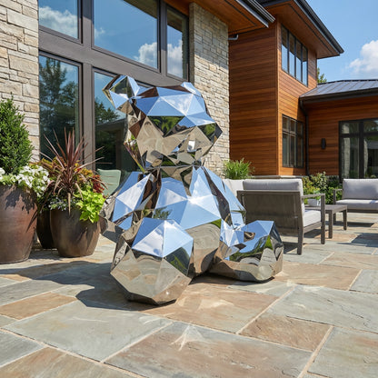 The Polish Sitting Bear by Landmark Decor, a striking faceted metallic sculpture, sits on a stone patio with outdoor seating and potted plants, in front of a modern house with large windows.