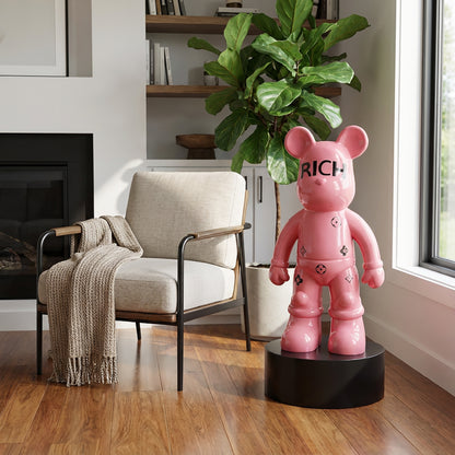 A modern living room features a Landmark Decor Rich Bear sculpture on a black pedestal, beige armchair, tan blanket, and potted plant—ideal for anyone who loves artistic sculptures in their decor.