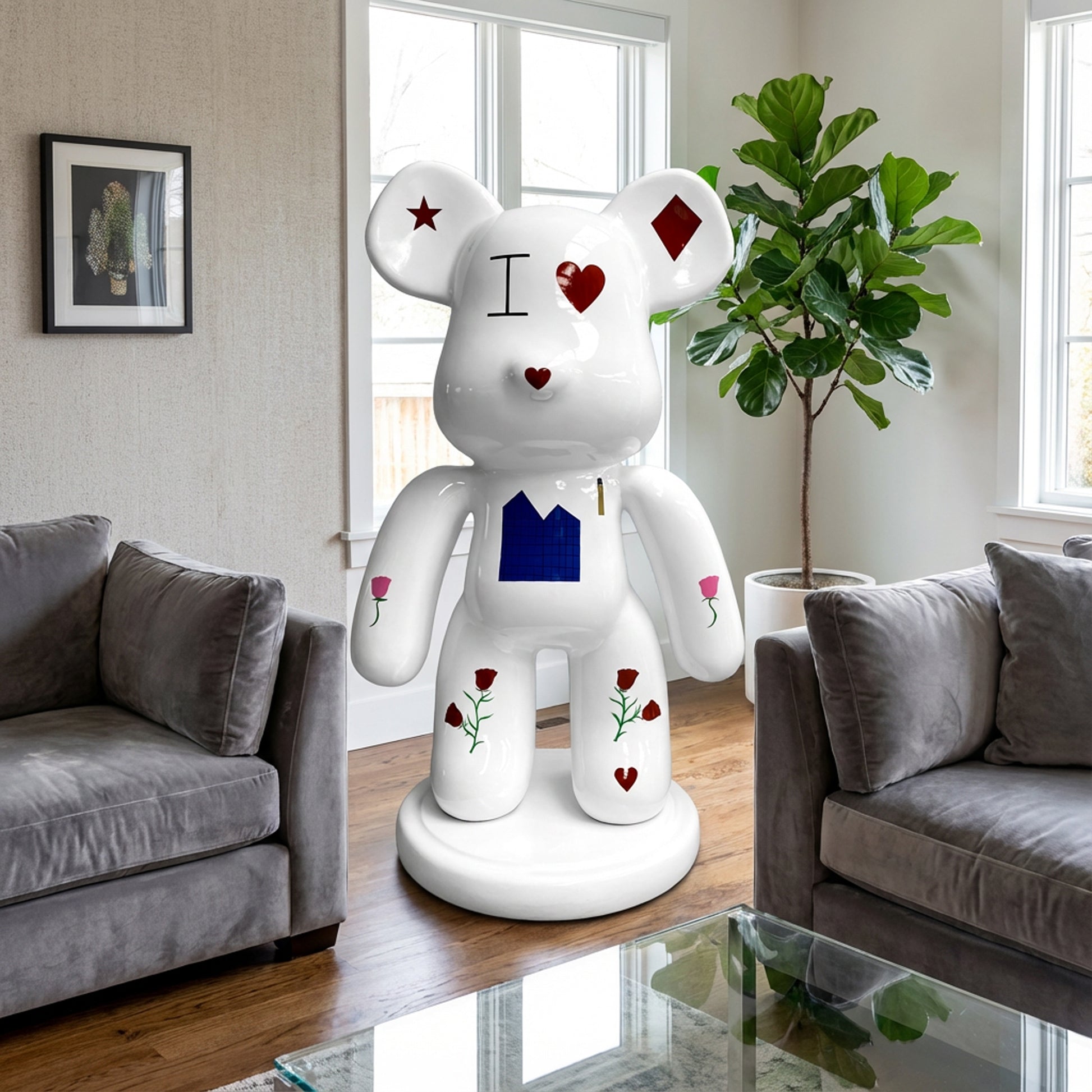 The Landmark Decor Violent Bear, a large white statue with red, black, and blue designs, stands between two gray sofas and next to a green plant, bringing an artistic sculpture accent to your living room decor.