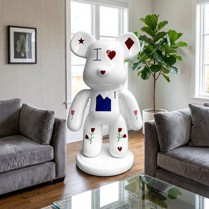 The Landmark Decor Violent Bear, a large white statue with red, black, and blue designs, stands between two gray sofas and next to a green plant, bringing an artistic sculpture accent to your living room decor.