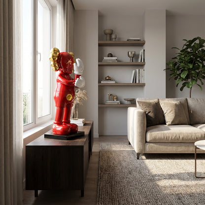 A modern living room with neutral tones features the SMH red pop art-style figurine by Landmark Decor on a dark wood console near a large window, with books and other Landmark Decor accents completing the sophisticated space.
