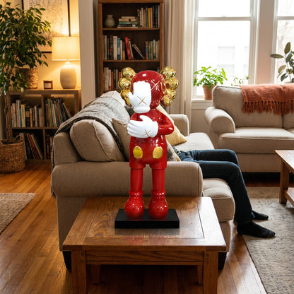The SMH statue by Landmark Decor, a large red cartoon-like piece with gold ears, stands on a coffee table in a cozy living room where a person sits on the sofa, their legs visible.
