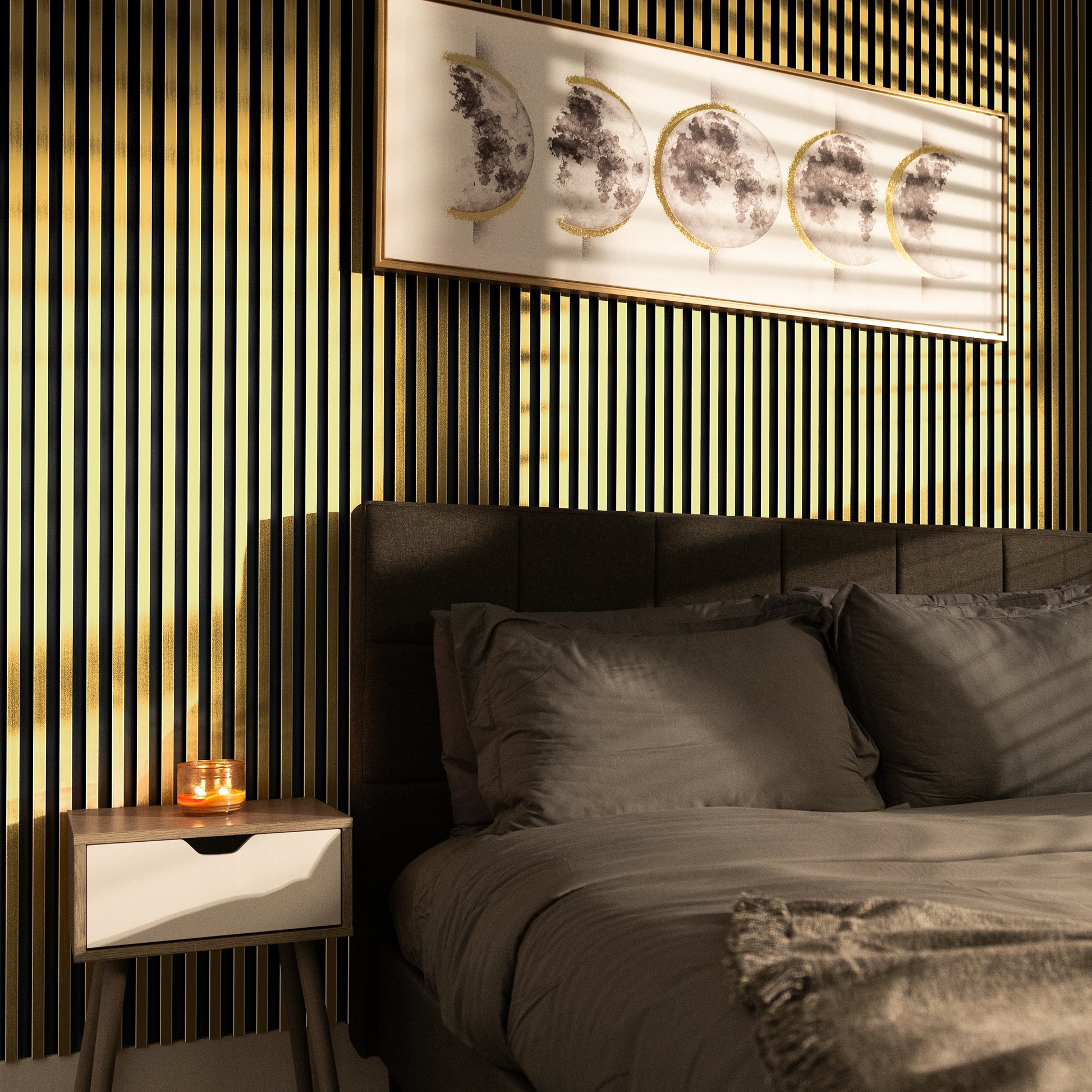 A neatly made bed with gray bedding sits next to a nightstand holding a lit candle; above the bed, moon phase artwork hangs on an accent wall featuring Landmark Decor's Bright Gold WPC Fluted Slat Wall Panel.