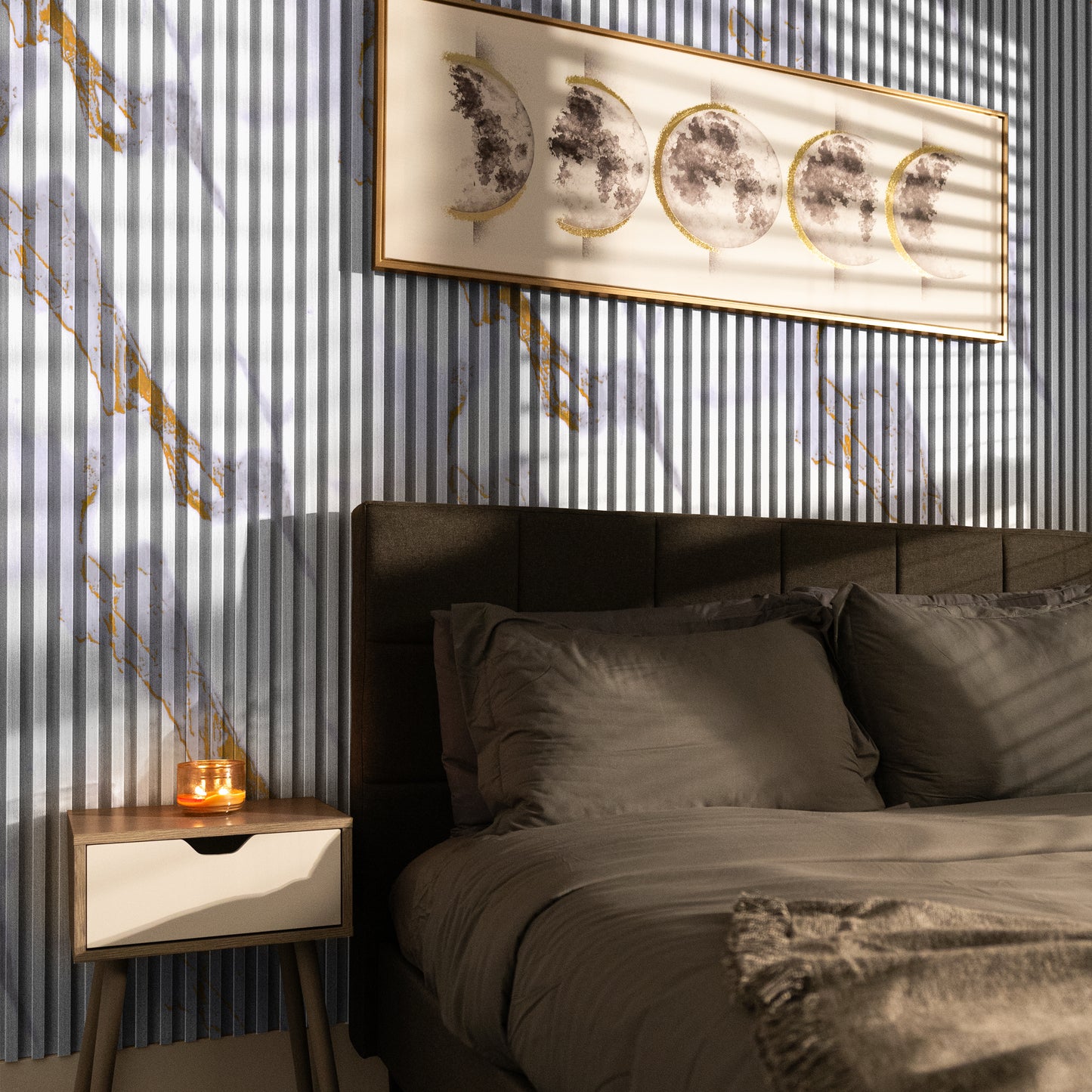 A neatly made bed with gray bedding sits beside a wooden nightstand and candle. Above, Landmark Decor's Calacatta Ember WPC Fluted Slat Wall Panel creates a striking backdrop, with sunlight casting soft shadows in the serene space.