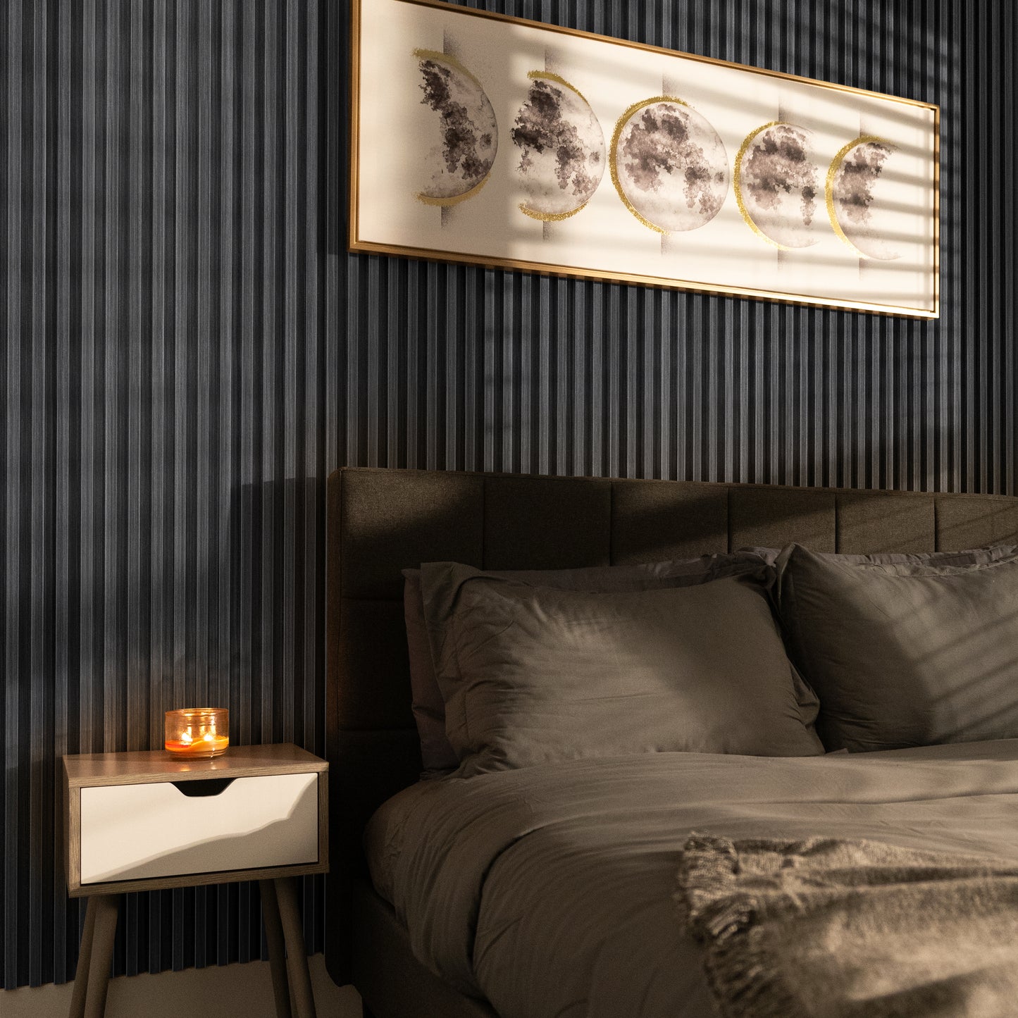 A modern bedroom featuring Landmark Decor's Graphite Strata WPC Fluted Slat Wall Panel as a dark accent wall, moon phase art, a bed with gray bedding, and a lit candle on the nightstand.