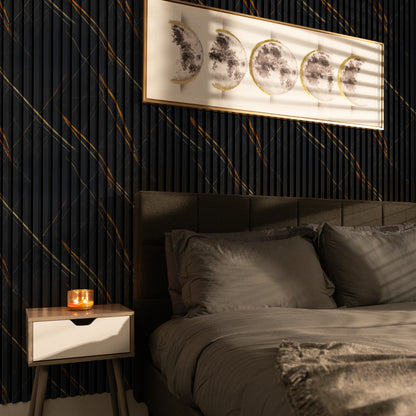 A candle rests on a wooden nightstand beside a neatly made bed with gray bedding; above, Landmark Decor’s Molten Nero Vein WPC Fluted Slat Wall Panel frames moon phase artwork and enhances the dark accent wall.