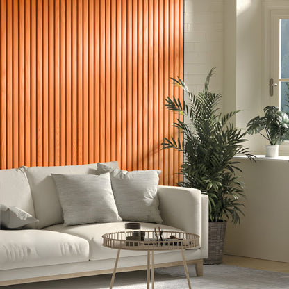 A modern living room with a beige sofa, light gray pillows, a round metal coffee table, potted plants, and an Orange WPC Fluted Slat Wall Panel by Landmark Decor accenting the sunlit window.