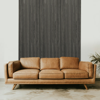 A tan leather sofa sits before the Landmark Decor Grey Oak Acoustic Slat Wall Panel, featuring real wood slats and a small green plant on the right—an elegant accent for modern interiors.