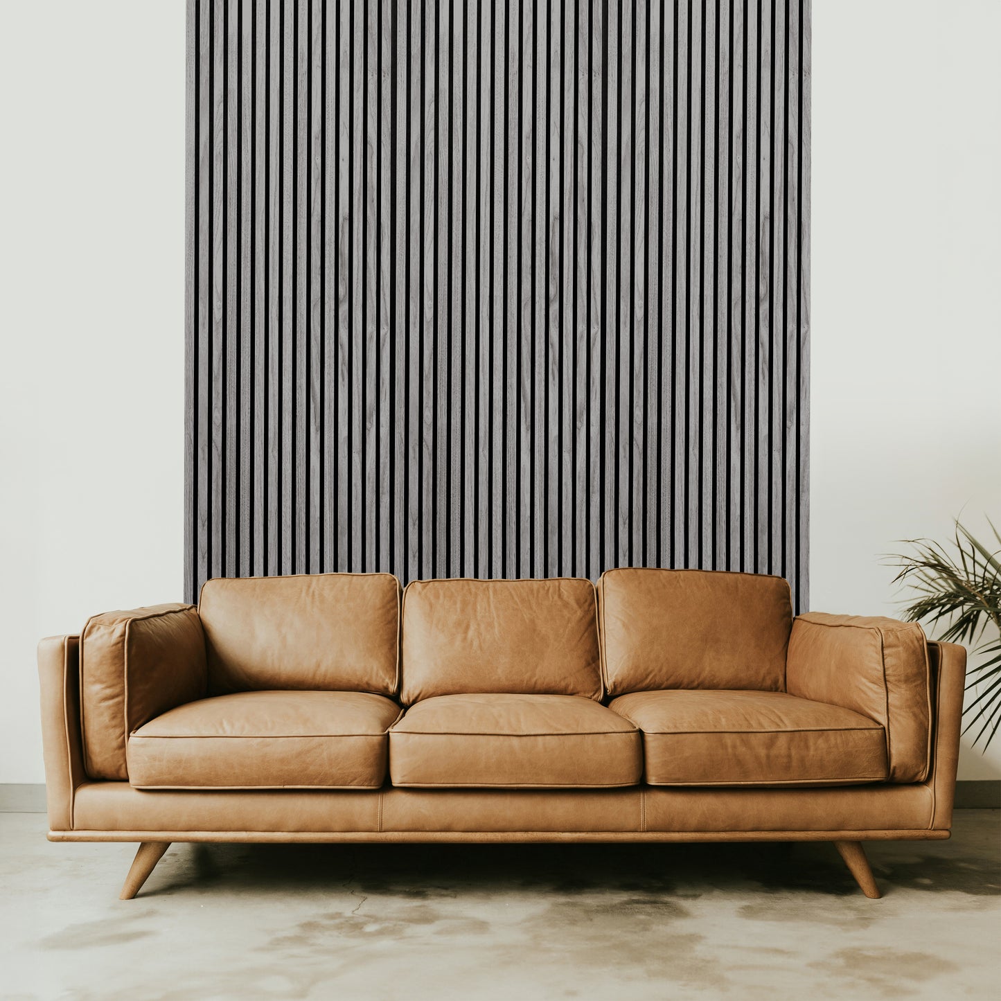 A tan leather sofa sits in front of a Landmark Decor Light Gray Acoustic Slat Wall Panel, with a plant partially visible on the right side.