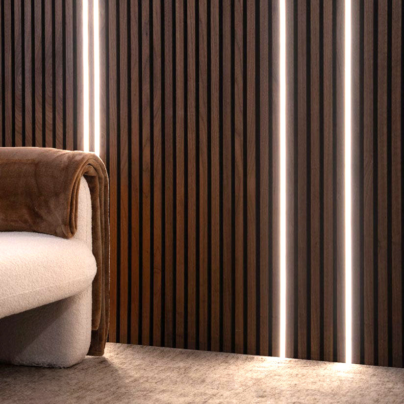 A white upholstered sofa with a brown blanket draped over the arm sits in front of Landmark Decor's Wood Panel LED Lights, where dark wood fluted wall panels are accented by vertical LED light strips to create an inviting ambient glow.